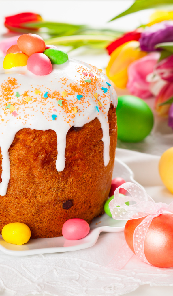 Красивый кулич с конфетами на столе с букетом тюльпанов и крашеными яйцами на Пасху