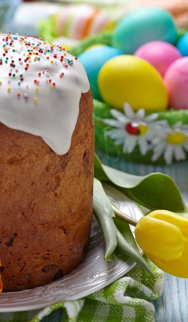 Пасхальный кулич на столе с тюльпанами и крашеными яйцами