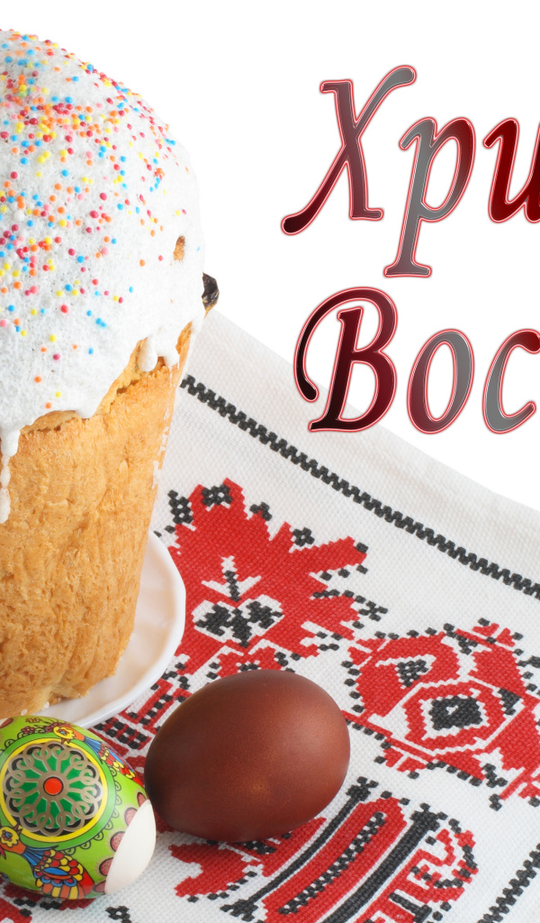 Пасхальный кулич с белой глазурью и крашеными яйцами на рушнике с надписью Христос Воскрес на белом фоне
