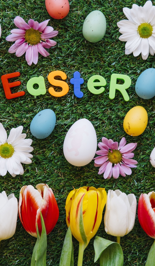 Надпись Easter на зеленой траве с крашеными яйцами и цветами