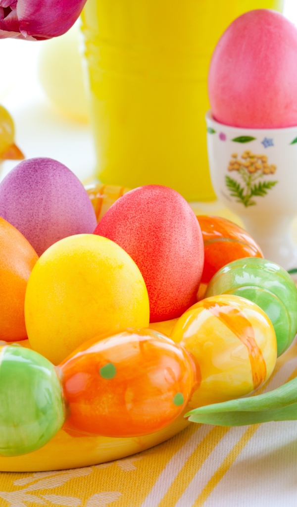 Разноцветные яйца с фигурками на столе с тюльпанами к Пасхе