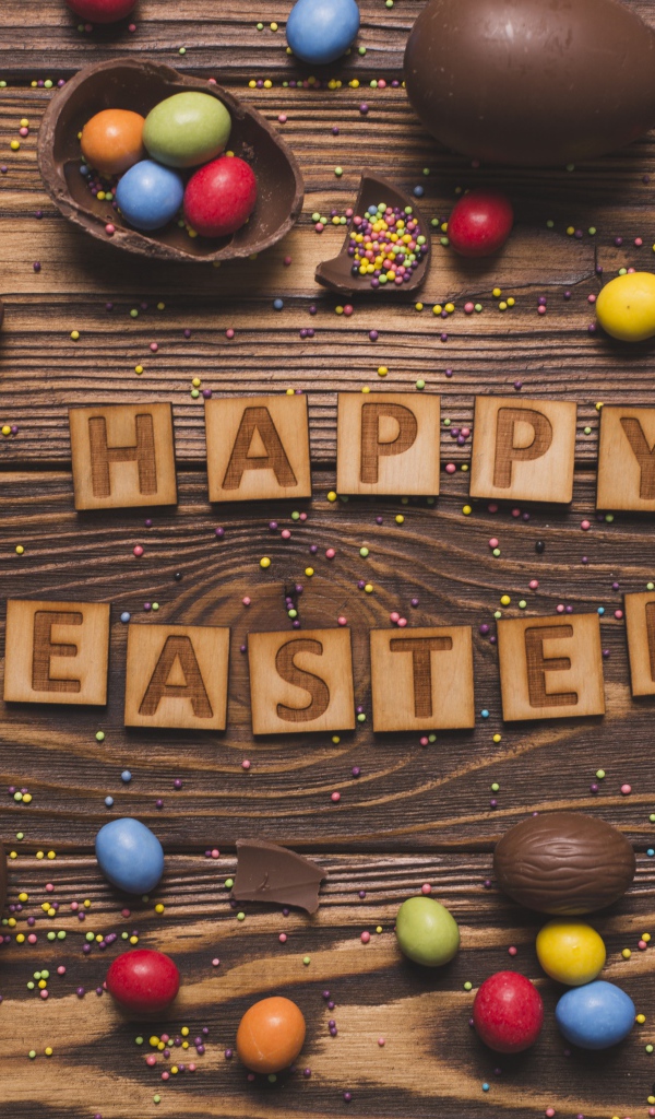 Надпись на английском Счастливой Пасхи на столе с шоколадными яйцами и конфетами
