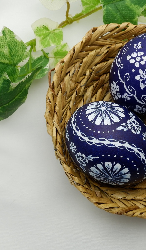 Три раскрашенных яйца в корзинке на столе с веткой 