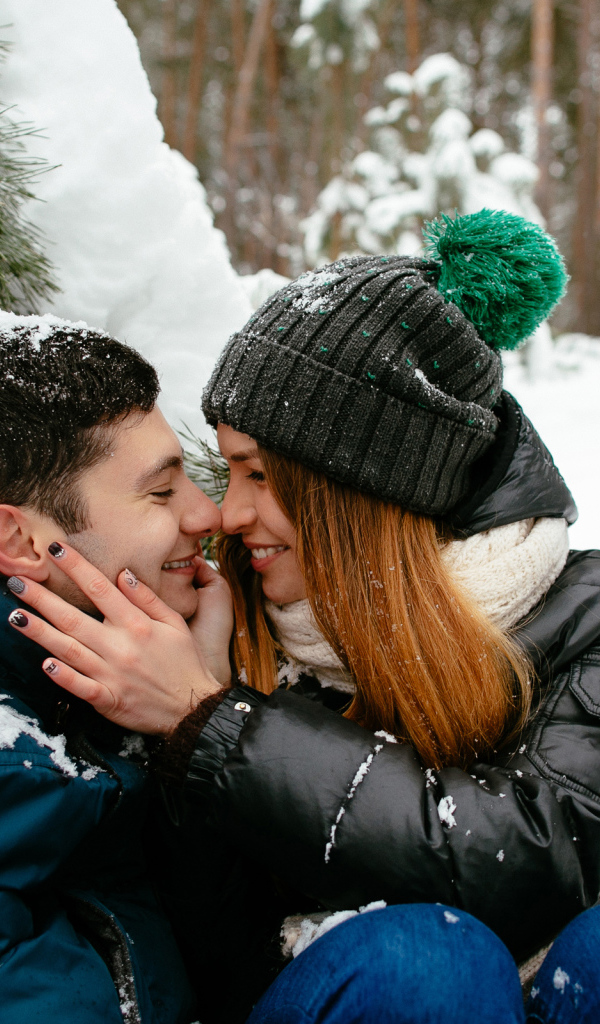 Влюбленная пара сидит под заснеженной еловой веткой зимой