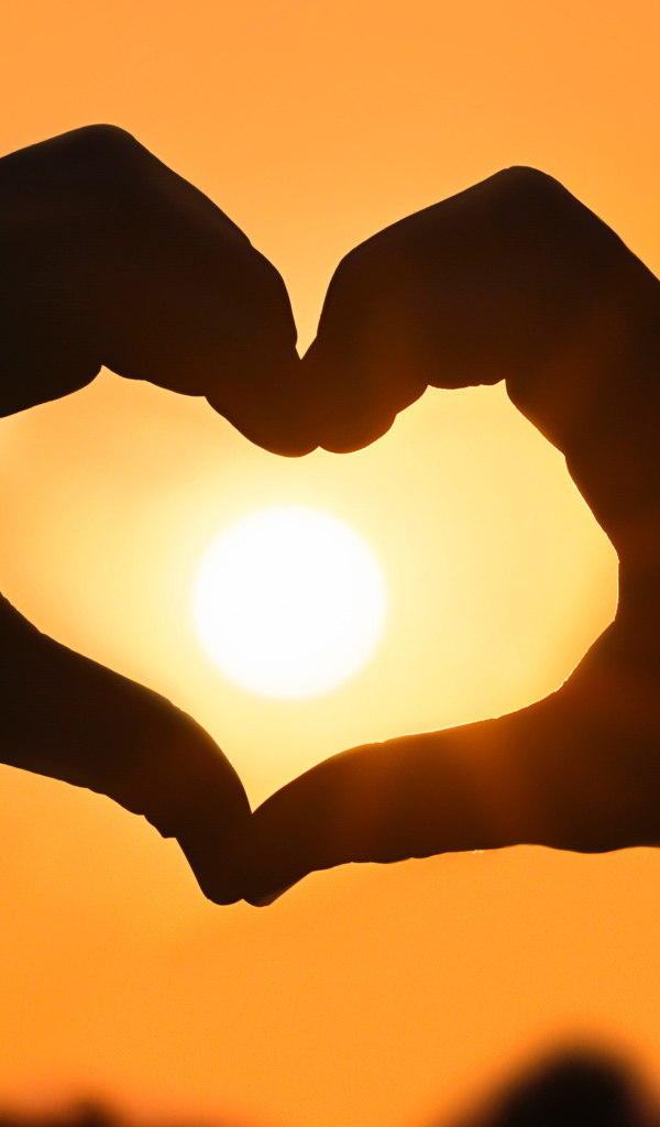 Сердце руками на фоне солнца в небе