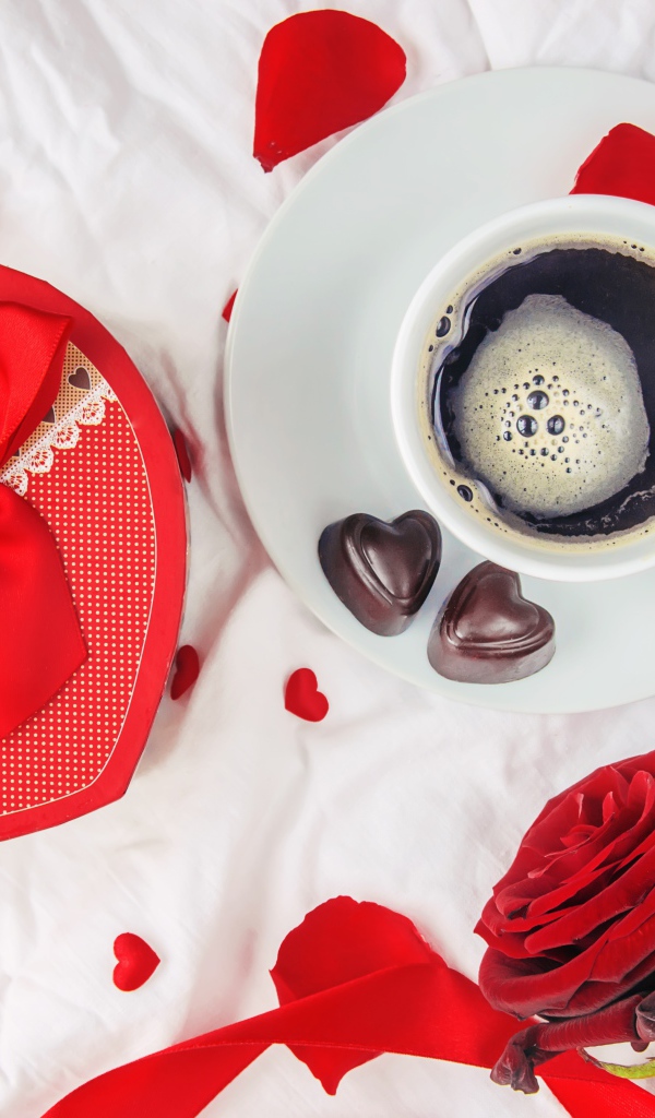 Кружка с кофе и шоколадными конфетами на столе с подарком и красной розой 