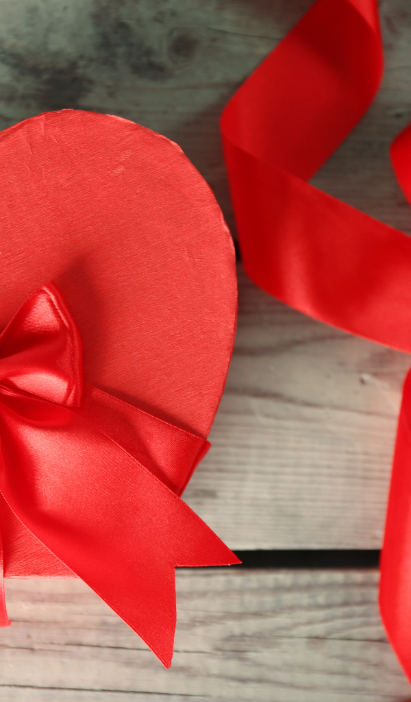 Красная коробка в форме сердца на деревянном столе с красными лентами