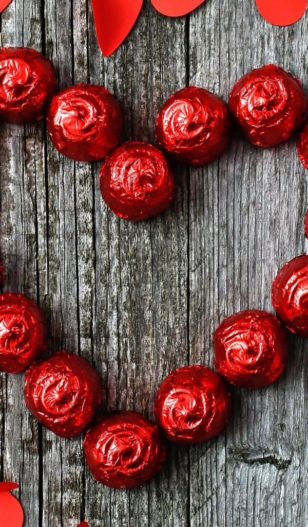 Красное сердце из конфет на деревянном фоне с бумажными сердечками