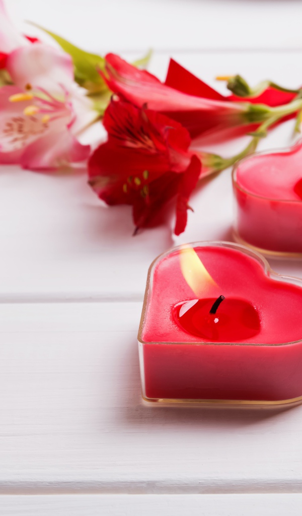 Две красные свечи в форме сердца на столе с цветами альстромерии 