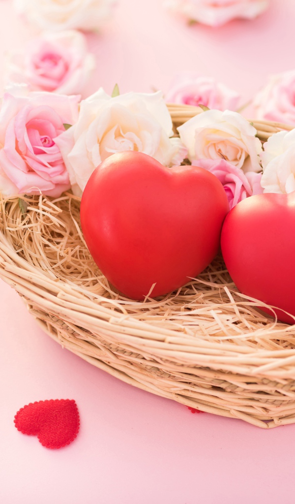 Two red hearts lie in a basket with roses