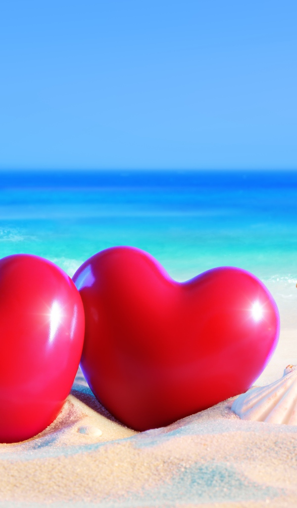 Два красных сердца на белом песке с ракушками на фоне моря