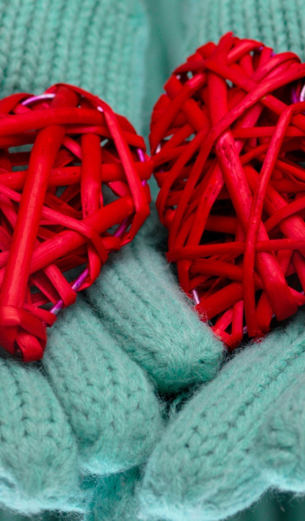 Два плетеных красных сердца лежать на руках в варежках