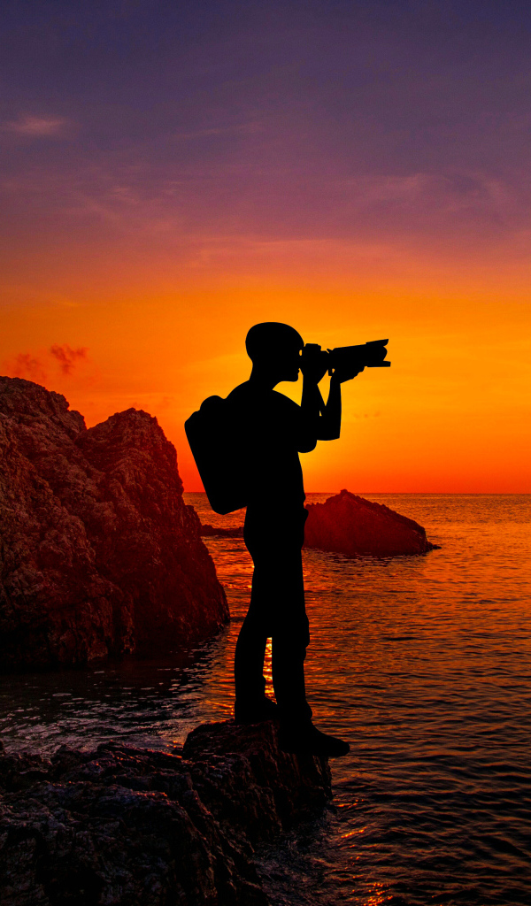 A man photographs a sunset by the sea
