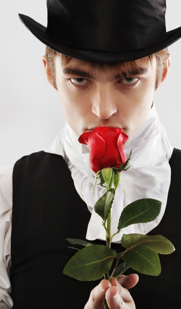 Парень в цилиндре с красной розой в руке на сером фоне