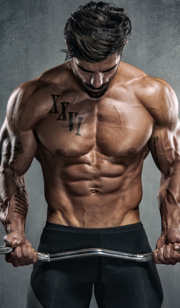 Накаченный мужчина с гантелей в руках на сером фоне