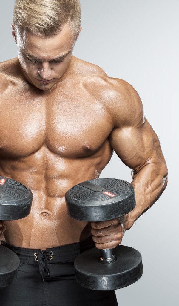 Накаченный мужчина с гантелями в руках на сером фоне