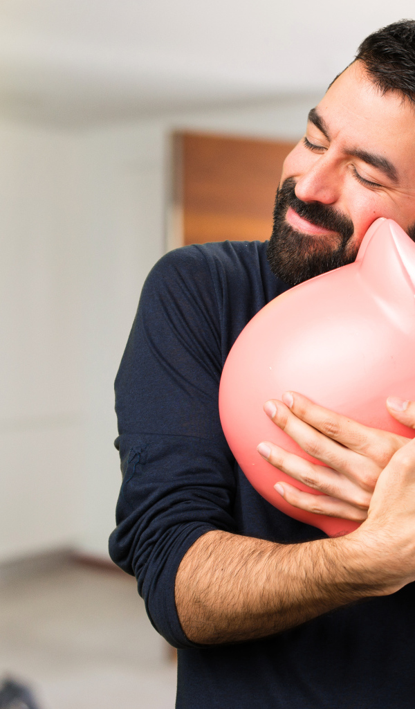 Мужчина обнимает розовую свинью копилку 