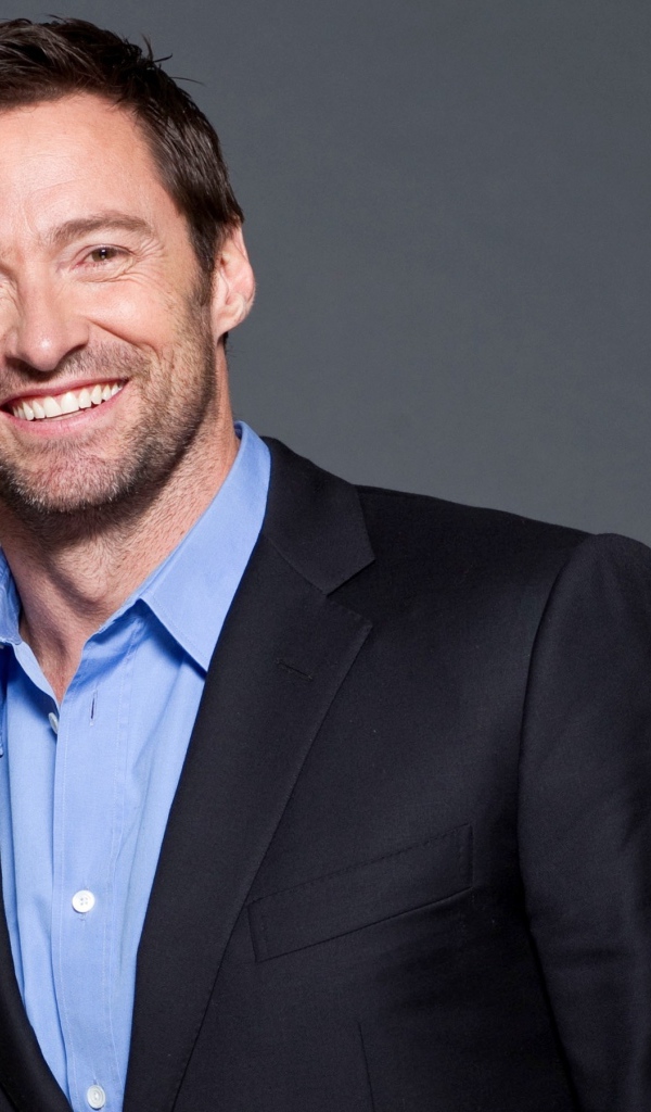 Улыбающийся мужчина, актер Хью Джекман  в костюме на сером фоне