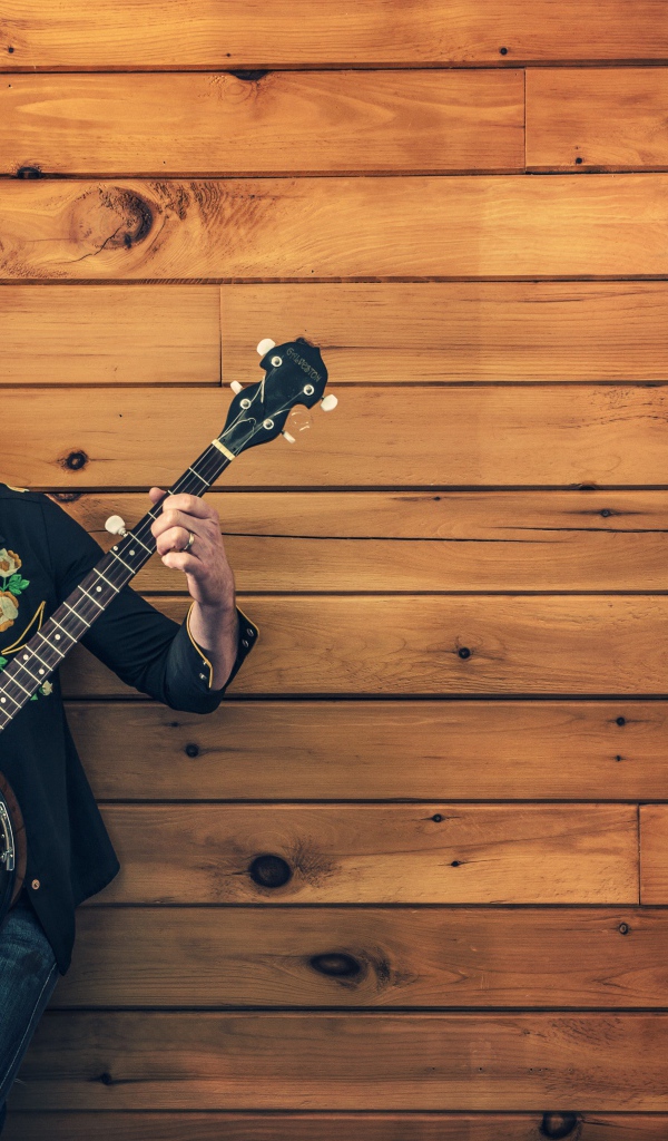 Парень музыкант играет на банджо у деревянной стены