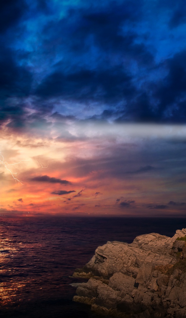 Маяк на берегу моря освещает грозовое небо 