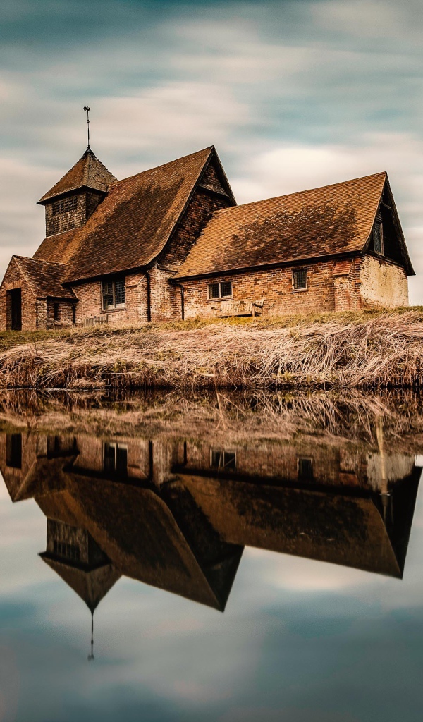 Старый дом на берегу реки отражается в воде