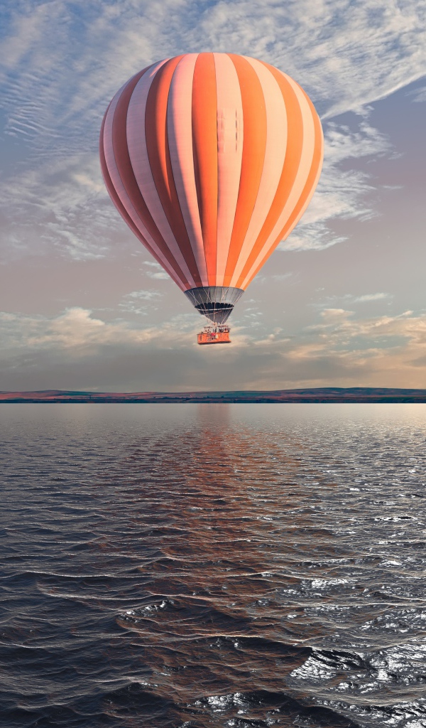 Большой оранжевый воздушный шар в небе над спокойной водой 