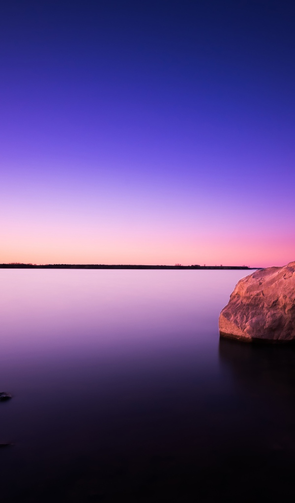 Большой камень в спокойной воде в сумерках