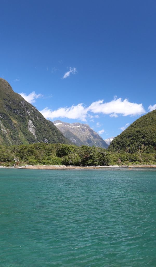 Голубая вода в озере на фоне покрытых зеленью гор под голубым небом