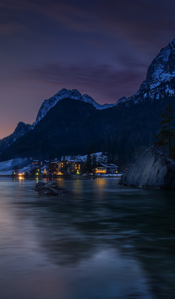 Город у озера на фоне заснеженных гор ночью 