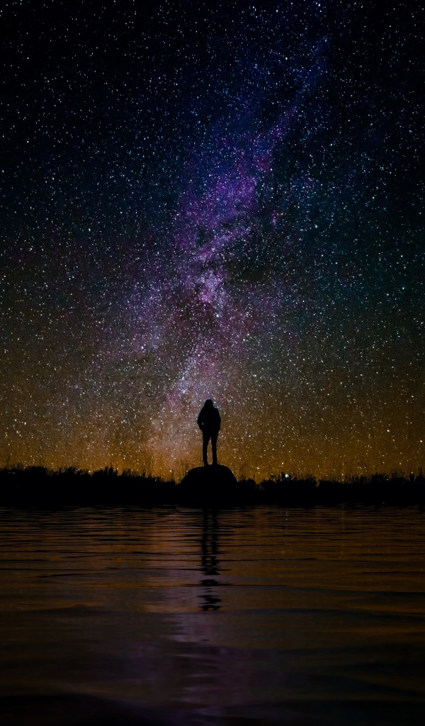 Силуэт человека стоит на камне у воды под звездным небом