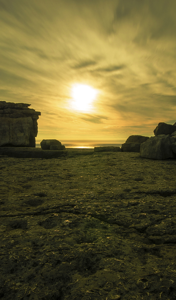 The sun in the clouds illuminates the stones by the sea