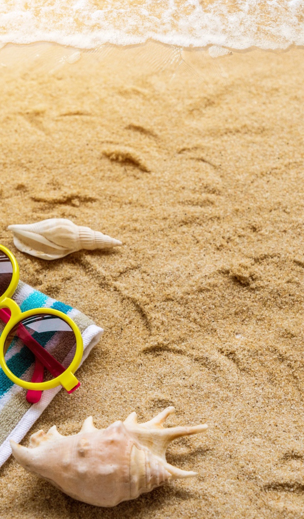Шляпа, очки, полотенце и ракушки на желтом песке у моря
