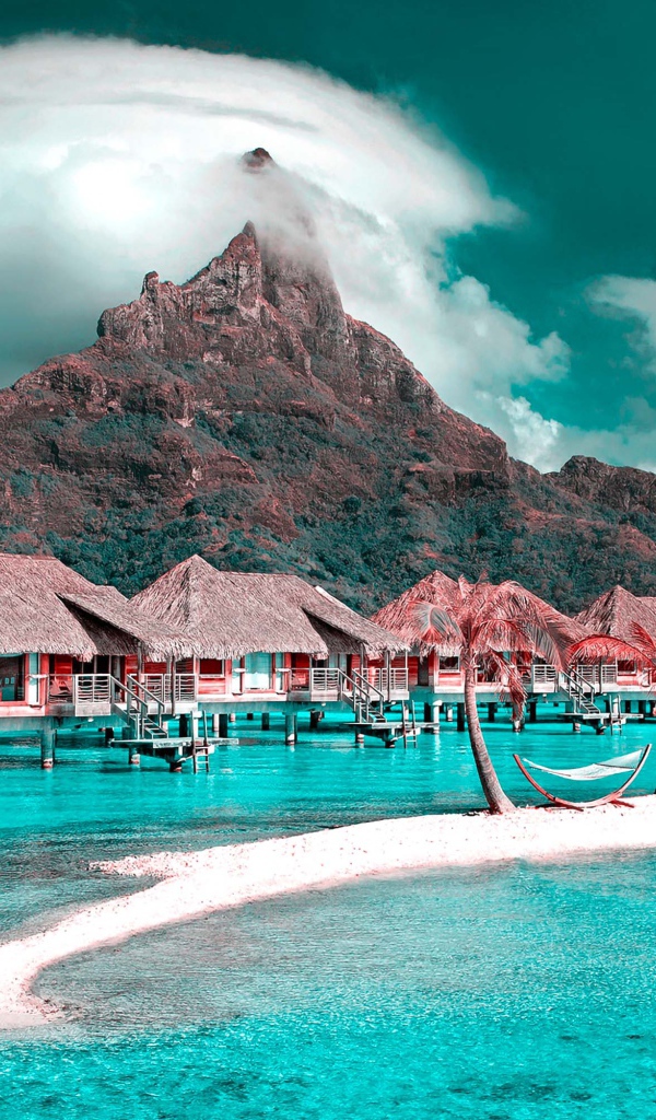 Дома на сваях в голубом океане на фоне горы под белыми облаками