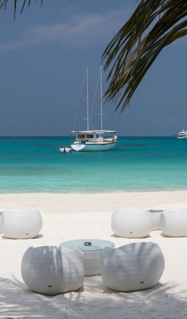 Белые кресла и столики на белом песке на пляже у голубой воды
