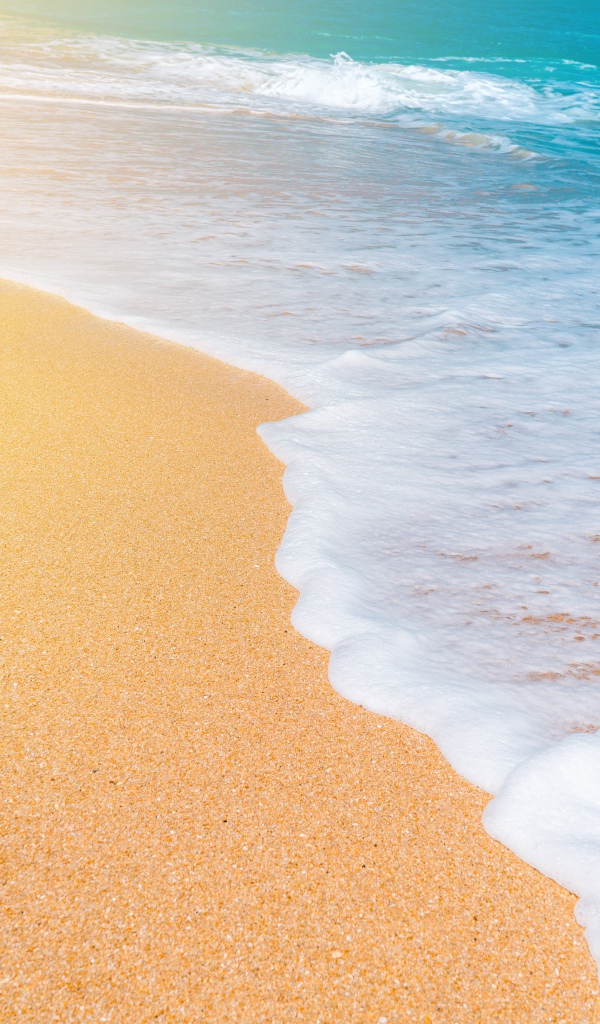 Белые волны океана омывают желтый горячий песок на пляже