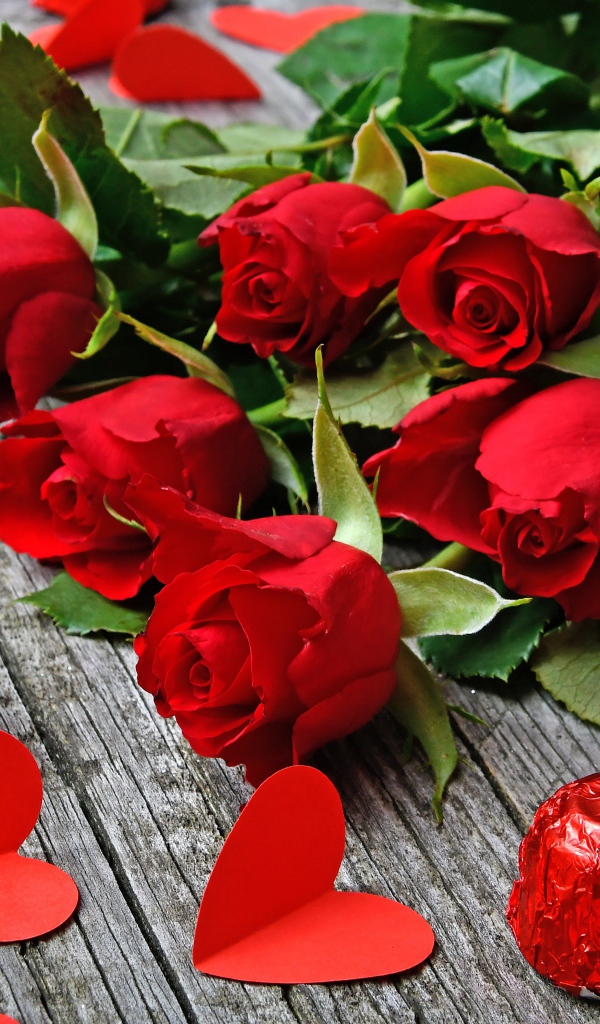 Букет красных роз на деревянном столе с конфетами и красными сердечками