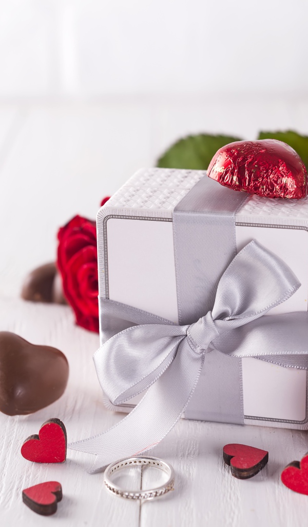 Подарок на столе с конфетами и букетом красных роз 