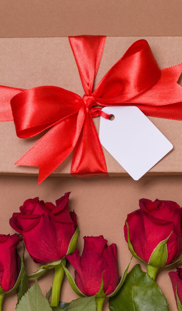 Подарок с красным бантом на бежевом фоне с красными розами