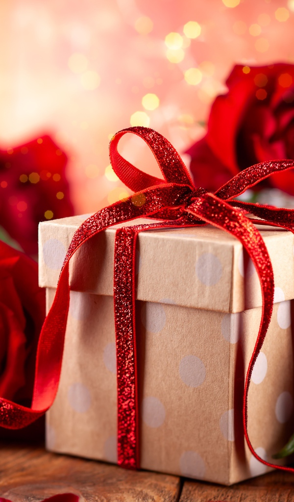 Подарок с красным бантом на столе с букетом роз