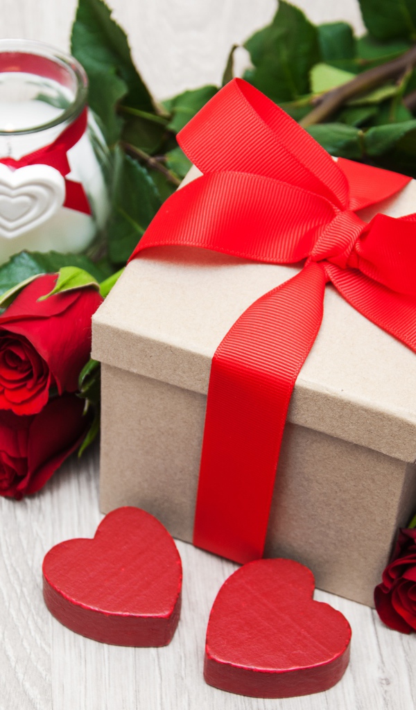 Красивый букет красных роз на столе со свечой и подарком