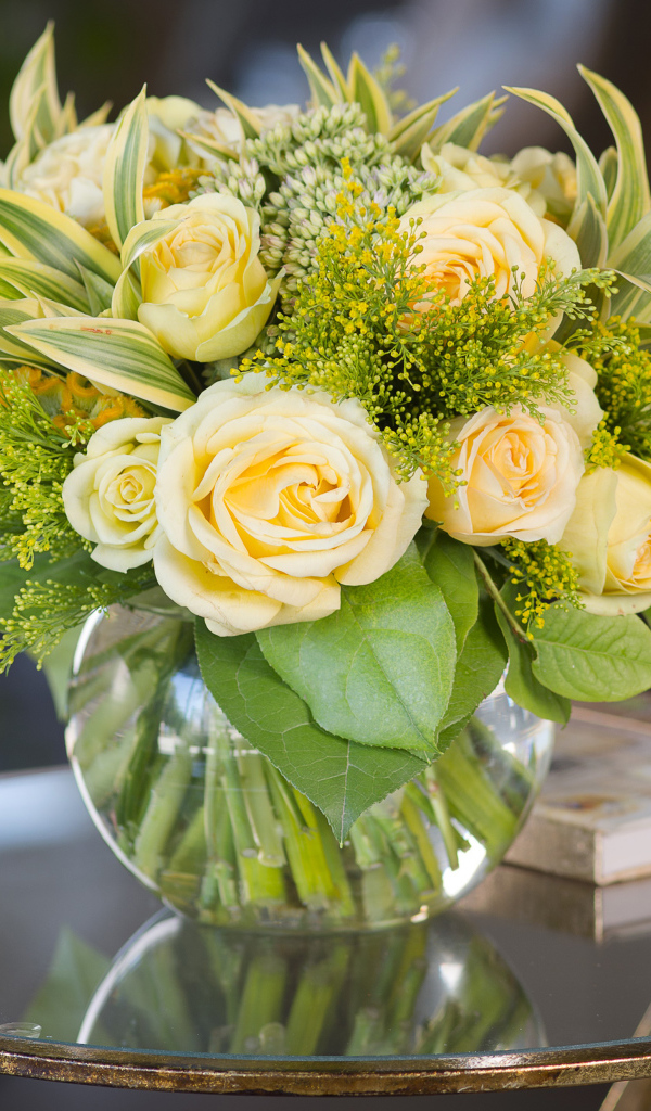 Красивый букет роз с зелеными листьями в в вазе на стеклянном столе