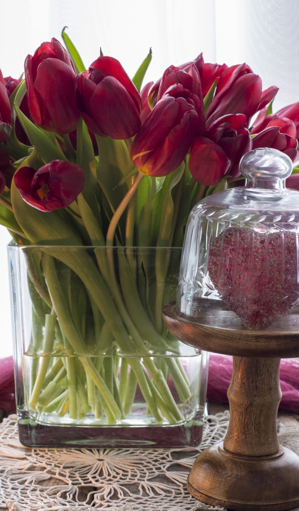 Букет красных тюльпанов в стеклянной вазе на столе со свечой и сердцем 