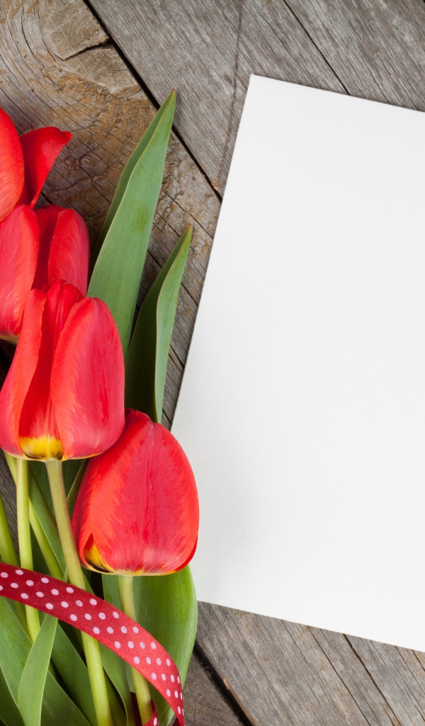 Букет красных тюльпанов с листом бумаги на деревянном столе