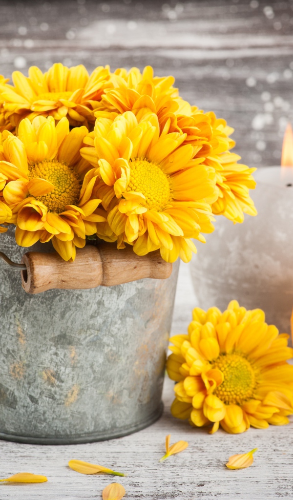 Букет желтых хризантем в ведерке на столе со свечами