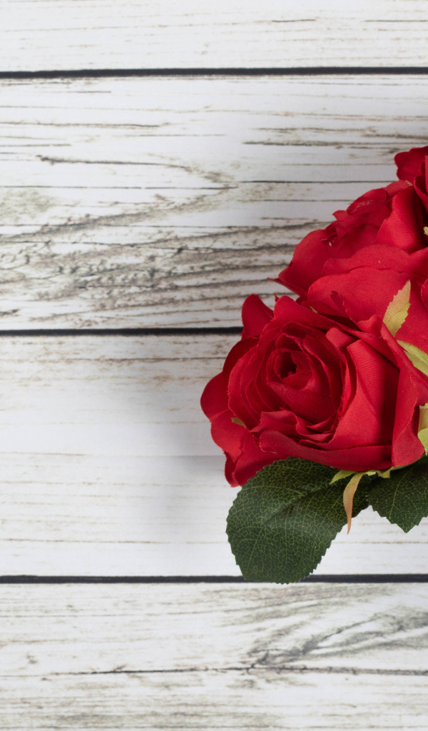 Три искусственные красные розы на деревянном фоне