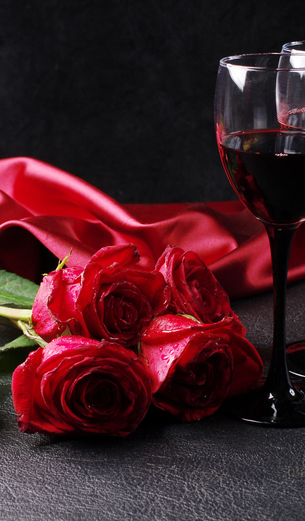 Два бокала с красным вином на черном фоне с букетом красных роз