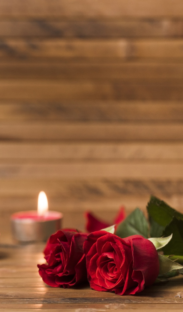 Две красные розы на столе с зажженными свечами 
