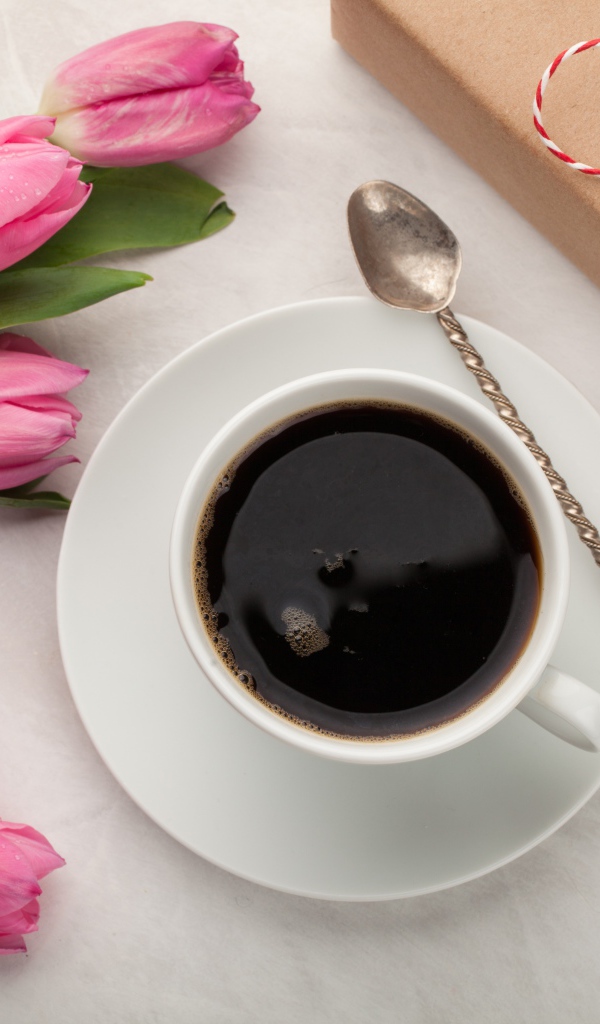 Белая чашка кофе на столе букетом розовых тюльпанов и подарком