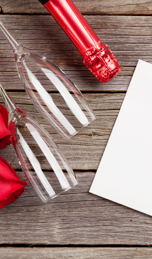 Белый лист бумаги на деревянном столе с бокалами и красными розами