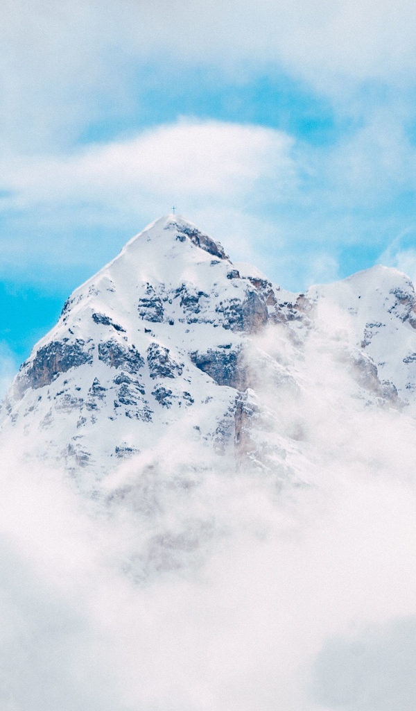 Snow-capped mountain peak in white clouds under blue sky